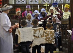 The Angel of the Lord has come the stable holding a large lamb bone to see the baby Jesus with Mary and Joseph as the Kings, shepherds and sheep look on